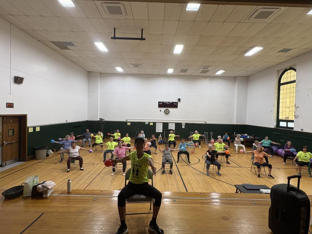 Club 99 participants exercising with small medicine ball in chairs at Evans Senior Center